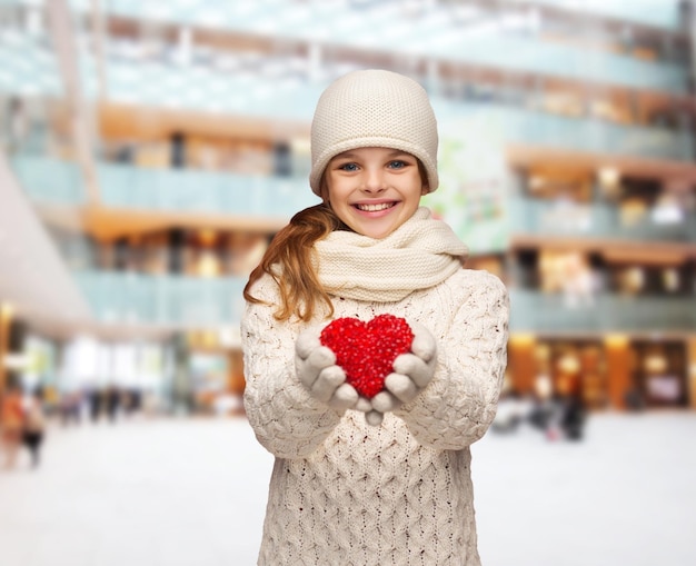 Kerstmis, vakantie, jeugd, cadeaus en mensenconcept - dromend meisje in winterkleren met rood hart over blauwe lichtenachtergrond