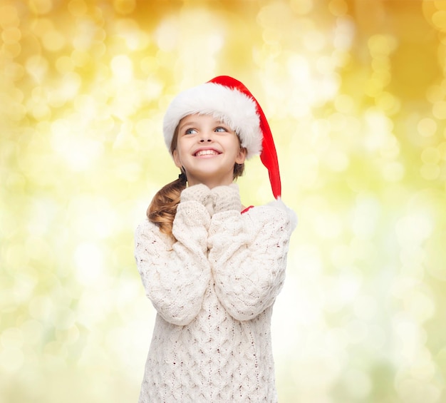 Kerstmis, vakantie, jeugd en mensen concept - lachend meisje in santa helper hoed over gele lichten achtergrond