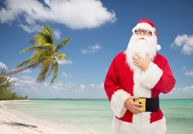 Kerstmis, vakantie, reizen en mensen concept - man in kostuum van de kerstman over tropisch strand achtergrond