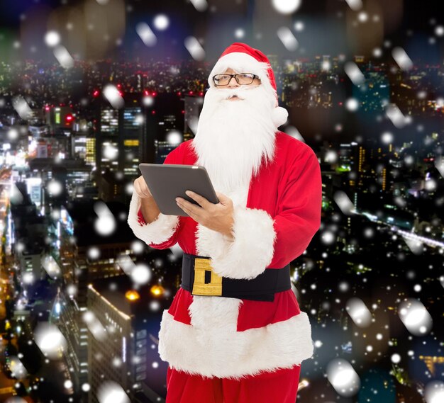 Kerstmis, vakantie, technologie en mensen concept - man in kostuum van de kerstman met tablet pc-computer over besneeuwde nacht stad achtergrond