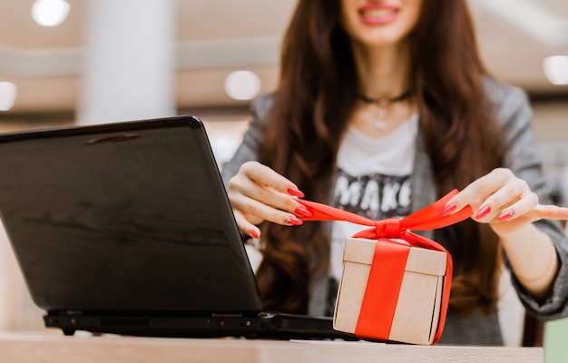 Kerstmis, vakantie, technologie en winkelconcept - lachende vrouw met creditcard op tafel, geschenkdoos en laptopcomputer. Horizontale foto