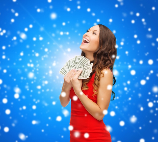 Kerstmis, vakantie, verkoop, bankieren en mensenconcept - glimlachende vrouw in rode kleding met ons dollargeld over blauwe besneeuwde achtergrond