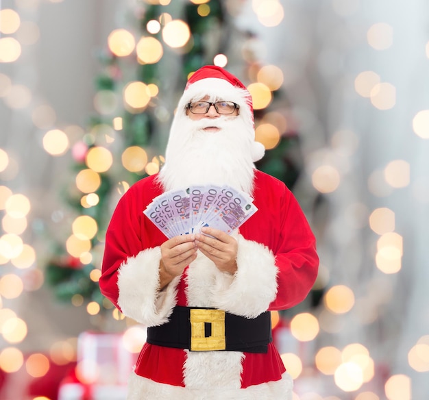 Kerstmis, vakantie, winnen, valuta en mensen concept - man in kostuum van de kerstman met euro geld over boom lichten achtergrond