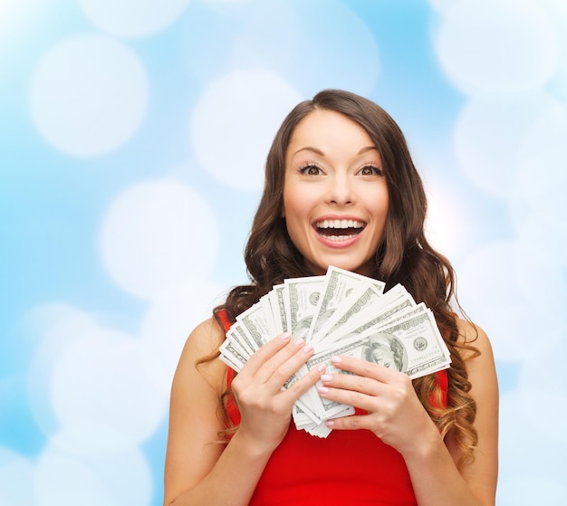 Kerstmis, verkoop, bankieren, winnen en vakantieconcept - glimlachende vrouw in rode kleding met ons dollargeld over blauwe lichtenachtergrond