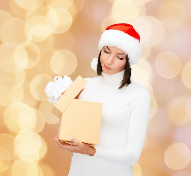 Kerstmis, winter, geluk, vakantie en mensen concept - vrouw in santa helper hoed met geschenkdoos over beige lichten achtergrond