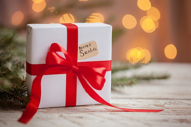 Kerstmis wit vakje of heden met rood lint voor geheime santa op houten tafel.