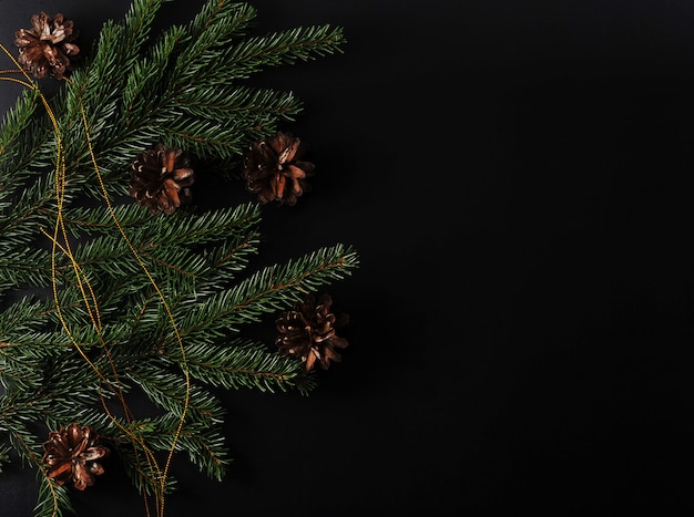 Kerstmisachtergrond met nette takjes en kegels op zwarte achtergrond met plaats voor tekst en groeten met hoogste mening