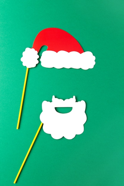 Kerstmisdecoratie, witte baard en rode Santas-hoed op stokken op groene achtergrond