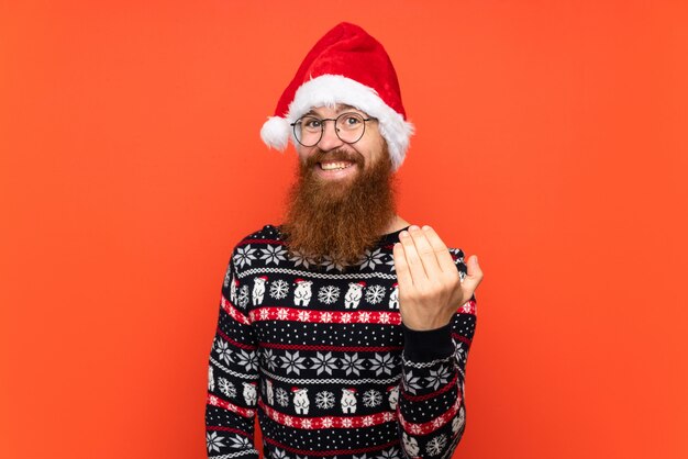 Kerstmismens met lange baard over geïsoleerde rode muur die met hand uitnodigt te komen. Blij dat je bent gekomen