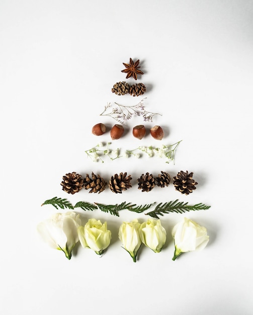 Kerstmissamenstelling in vorm van Kerstboom met takken van thuja, bloemen, noten en kegels. Plat leggen