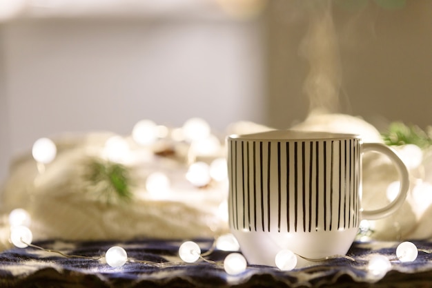 Foto kerstmissamenstelling met kop warme drank, lichtgevende garland, witte sweater op oppervlakte, exemplaarruimte. gezellig huis.