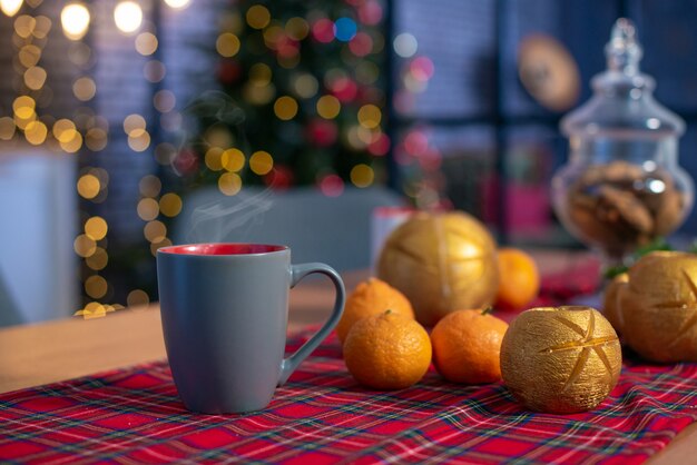 Kerstmissamenstelling met mandarijnen en een kop thee. Nieuwjaar huis kamer met boom en feestelijke bokeh verlichting.