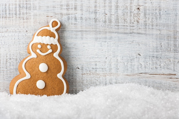 Kerstmissneeuwman-vormige koekjespeperkoek op sneeuw en houten achtergrond