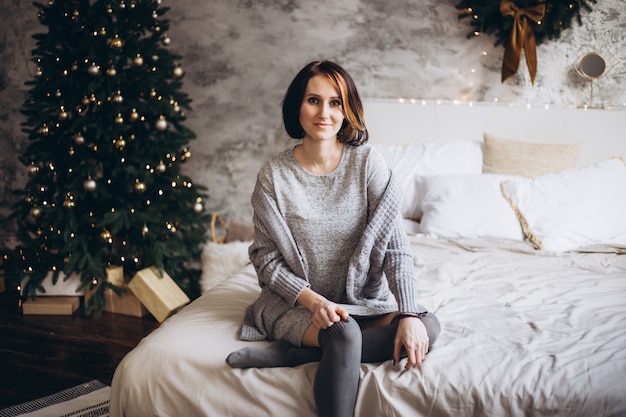 Kerstmisvrouw dichtbij een kerstboom op bed thuis