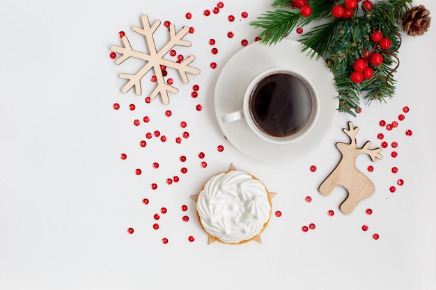 Kerstontbijt met een kopje koffie en een witte meringue-taart, op een witte tafel met nieuwjaarsdecor: houten speelgoed, een sneeuwvlok, een hert, een vuren tak. kopieer ruimte. bovenaanzicht