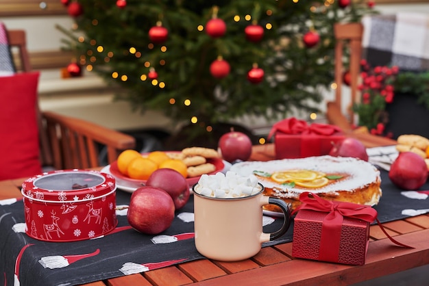 Kersttaart, cacao met marshmallows en tafel. Kerstboom achtergrond. Van mobiele aanhangwagen, stacaravan, terras. Nieuwjaarsviering. Kerstvakantie. Kerstochtend.