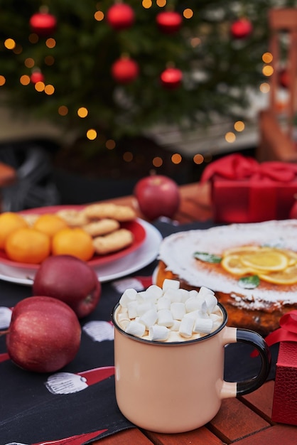 Kersttaart, cacao met marshmallows en tafel. Kerstboom achtergrond. Van mobiele aanhangwagen, stacaravan, terras. Nieuwjaarsviering. Kerstvakantie. Kerstochtend.