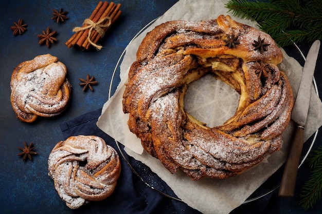 Kersttaartbroodje met kaneel en poedersuiker op een donkere oude betonnen of stenen achtergrond