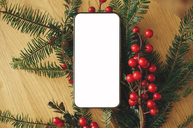 Kersttelefoon mock up flat lay Leeg scherm telefoon en dennen takken met rode bessen op rustieke houten tafel Ruimte voor tekst Kerst advertentie app sjabloon