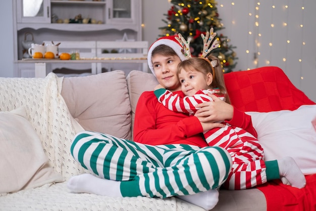 Kersttijd. schattige kinderen broer en zus in kerstpyjama knuffelen samen op de bank