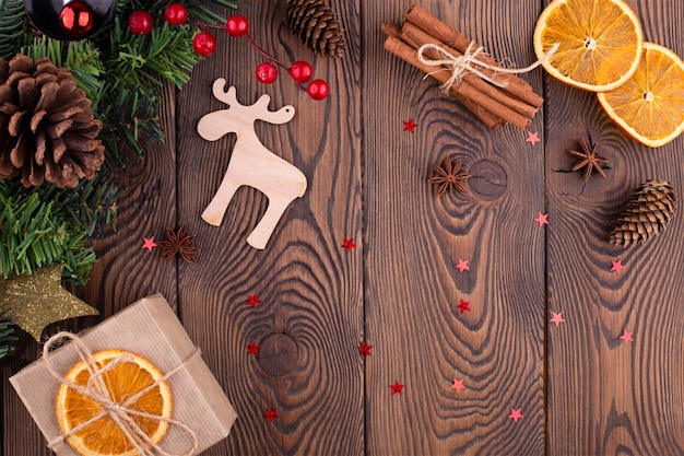 Kerstvakantie achtergrond met houten herten kerstboom versierd met dennenappel kralen en geschenken verpakt in ambachtelijke papier gedroogde sinaasappelen op houten achtergrond plat lag kopie ruimte