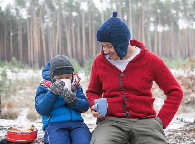 Kerstvakantie, vader en zoon die hete nieuwjaarsdrank drinken. Gelukkige familie op een wandeling buiten in het zonnige winterbos