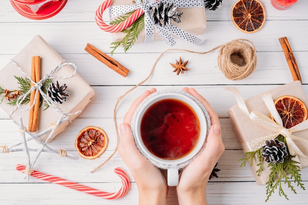 Kerstversiering met geschenkdozen, dennenappels en kopje thee in handen van de vrouw