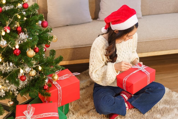 Kerstviering concept Jonge Aziatische vrouw zittend op de vloer en kerstcadeau openen