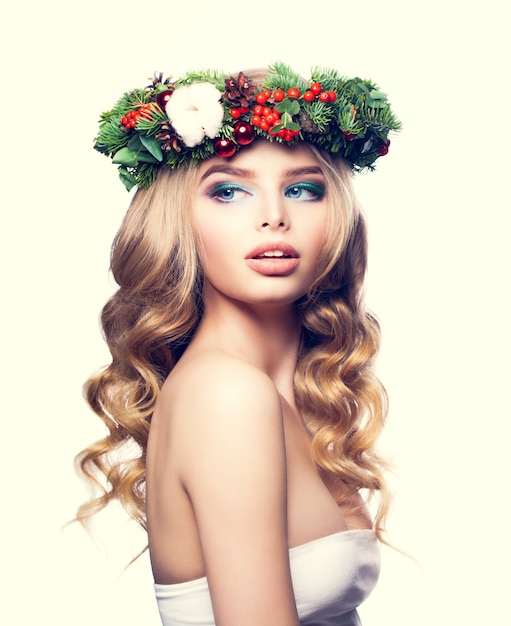 Kerstvrouw met make-up, blond krullend haar en bloemenkerstkrans. Jonge blonde schoonheid