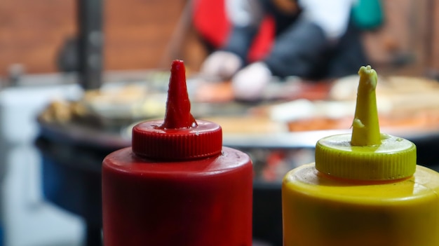 Ketchup en mayonaise in plastic buizen bij een straatgrill op de voorgrond close-up met selectieve focus. Barbecue, straatvoedselfestival. Twee blikjes vleessauzen. Rode en gele container.