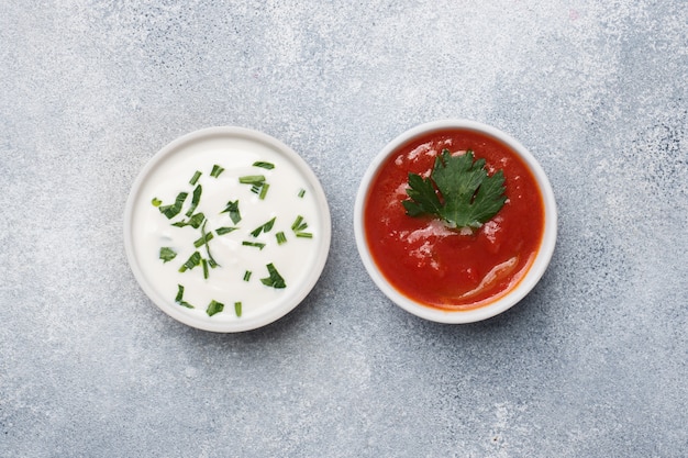 Ketchup mayonnaise greens in plates on a gray concrete table with copy space.