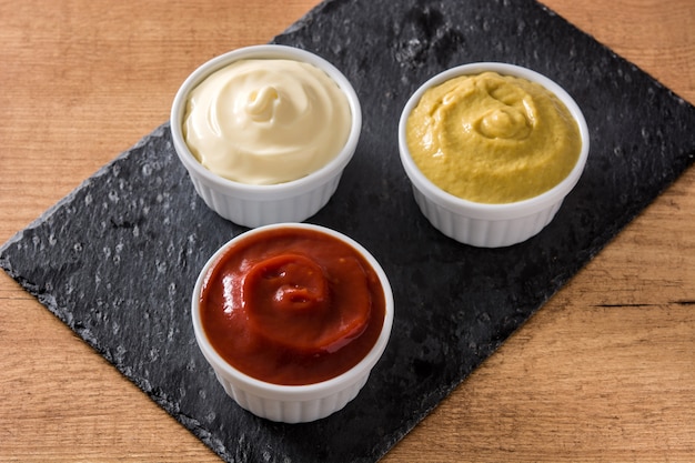 Ketchup, mosterd en mayonaise in kommen op zwarte leisteen