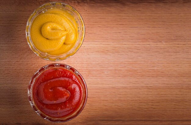 Ketchup and mustard in glass bowls on wooden table