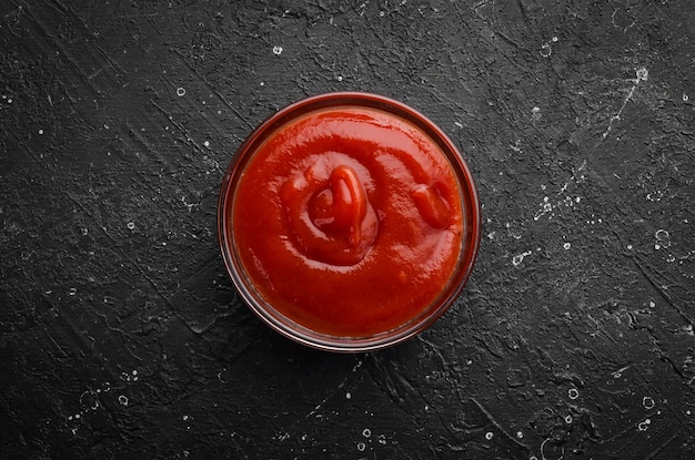 Ketchup sauce. Tomato paste in a bowl on a black stone background. Top view. Free copy space.