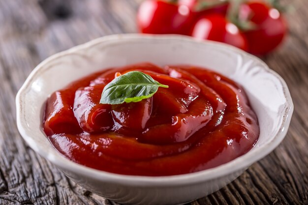 Ketchup or tomato sauce in white bowl and cherry tomatoes on wooden table.