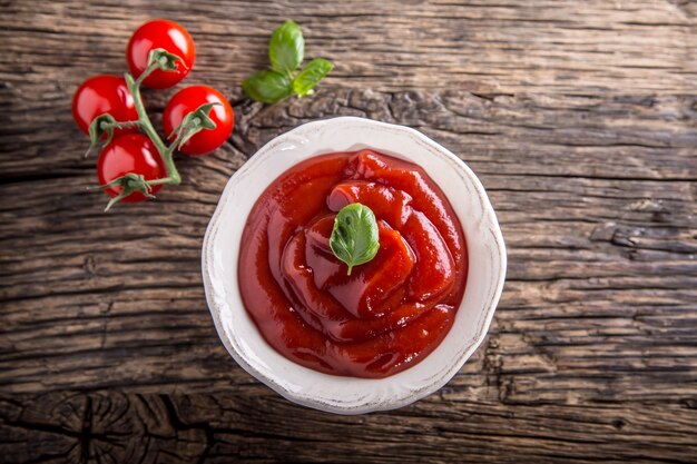 Кетчуп или томатный соус в белой миске и помидоры черри на деревянном столе.