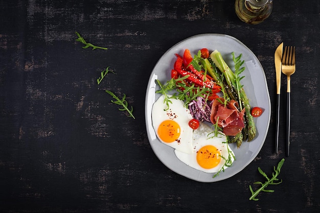 Keto breakfast Fried asparagus with roasted eggs and prosciutto or jamon Ketogenic diet Healthy food Top view flat lay