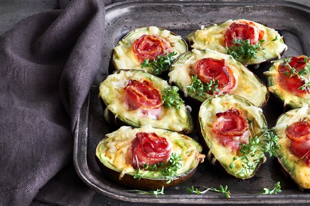 Keto-dieetgerecht: Avocado Boten met knapperig spek, gesmolten kaas en tuinkers op donker