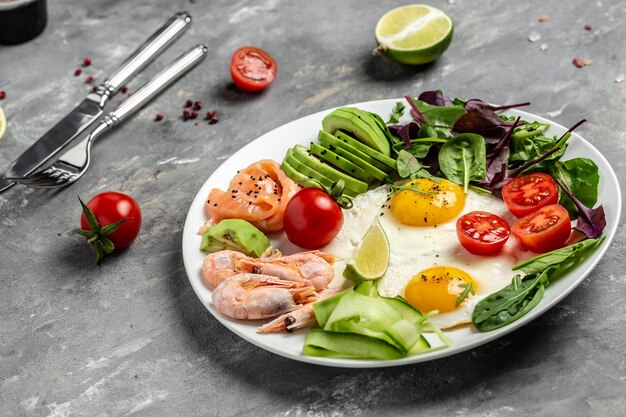 Keto-ontbijt met zalm, gekookte garnalen, gamba's, gebakken eieren, frisse salade, tomaten, komkommers en avocado. Concept van gezond eten.