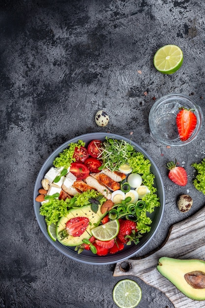 Ketogeen dieetvoer, kipfilet, quinoa, avocado, avocado, fetakaas, kwarteleitjes, aardbeien, noten en sla. gezond maaltijdconcept, verticaal beeld. bovenaanzicht. plaats voor tekst