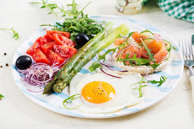 Ketogeen ontbijt Ontbijt Gebakken ei knapperige broden met zalm groene asperges verse tomaten en rode uien op witte plaat