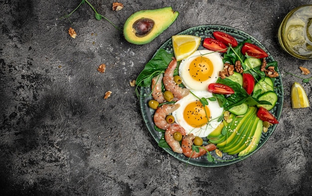 Ketogenic diet breakfast shrimps prawns soft fried egg fresh salad tomatoes cucumbers and avocado on a dark background Keto paleo lunch Top view