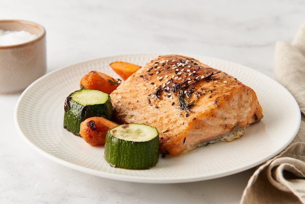 Кетогенный ужин с рыбным филе лосося с овощами на белой тарелке, вид сбоку крупным планом