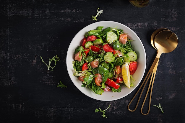 Фото Кетогенный салат с соленым лососем, лимоном, огурцами, оливками, помидорами, зеленым салатом и медово-горчичной заправкой. тренд здорового питания вид сверху