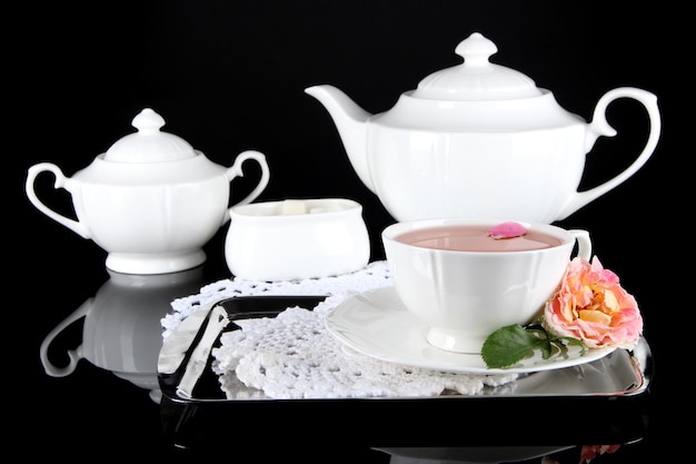 Photo kettle and cup of tea from tea rose on metallic tray on napkin black background