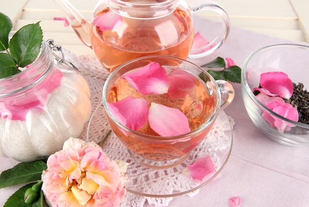 Kettle and cup of tea from tea rose on napkin on wooden background