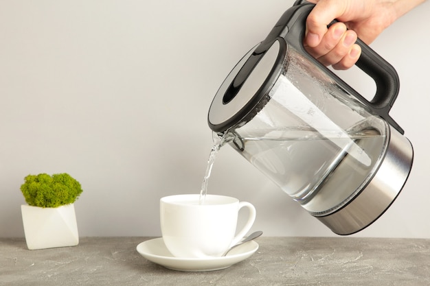 Photo kettle pouring boiling water into a cup on grey background. top view.