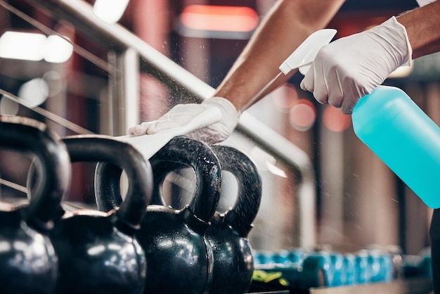 Kettlebell cleaning service and hands cleaning at a gym with liquid soap in spray bottle with cloth in gloves Janitor or cleaner wipes dirty bacteria on dusty weights or fitness training equipment