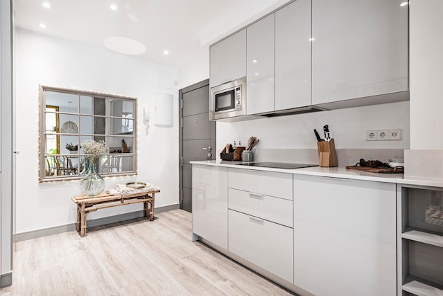 Keuken met grijs houten meubilair gecombineerd met wit stenen aanrechtblad en kleine apparatenkasten keramische kookplaat en magnetron naast de toegangsdeur naar een vakantieappartement