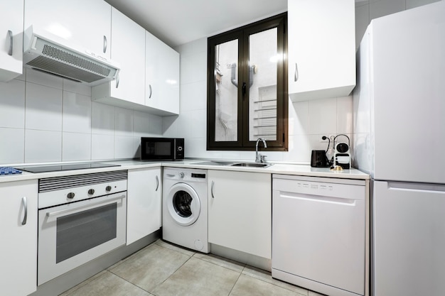 Keuken met wit gelakt meubel granieten aanrechtblad en porselein steengoed op de vloer en wanden en witte appliand